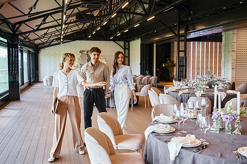 event manager showing festive tables to happy couple in love in event hall with wedding decor