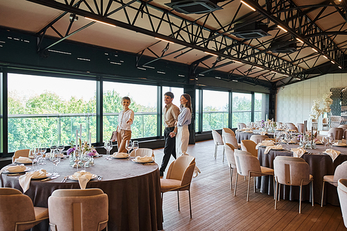 event organizer showing tables with festive setting to happy couple in decorated banquet hall