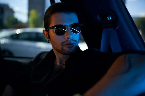 attractive young man in elegant black attire with sunglasses sitting in his car, sexy driver