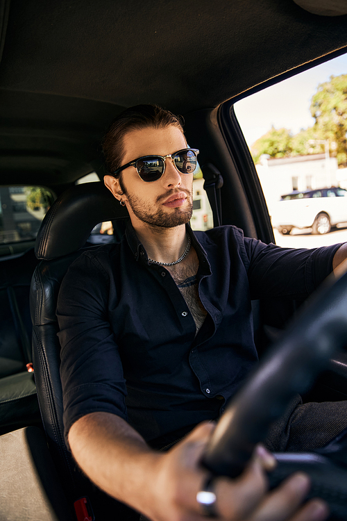 vertical shot of handsome elegant man with sunglasses sitting behind steering wheel, fashion concept