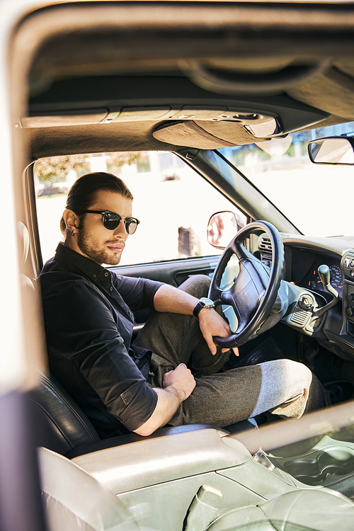 vertical shot of good looking sexy male model in stylish attire looking at camera at steering wheel