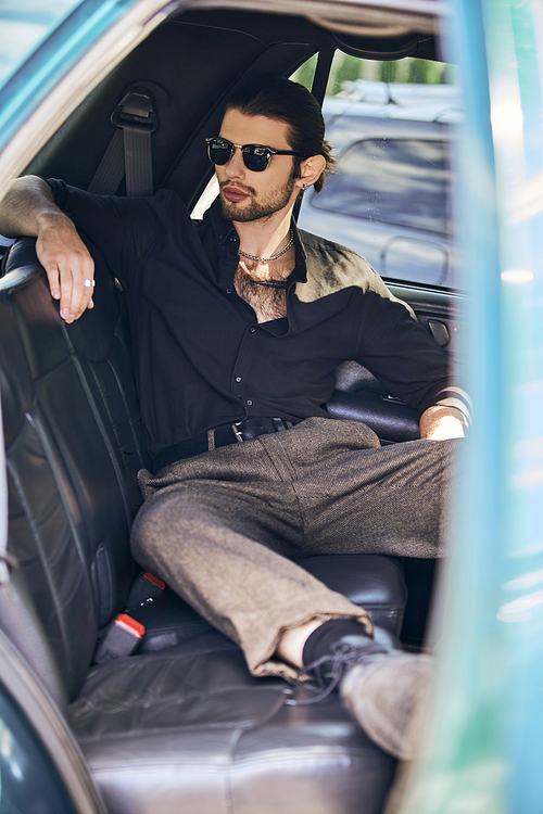 vertical shot of relaxed man in black elegant attire chilling behind steering wheel, sexy driver