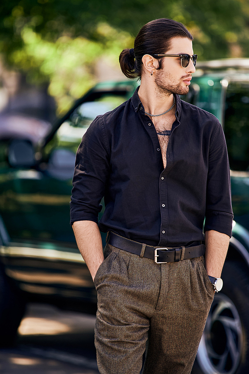 vertical shot of sexy young man with accessories with hands in pockets posing in front of his car