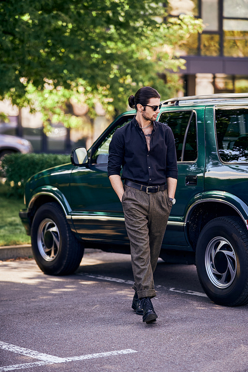 handsome sexy man with sunglasses in black shirt walking near his car and looking away, fashion
