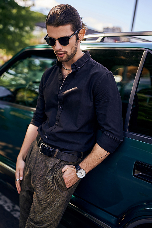 stylish sexy man in black shirt with sunglasses posing next to his car outdoors, fashion and style