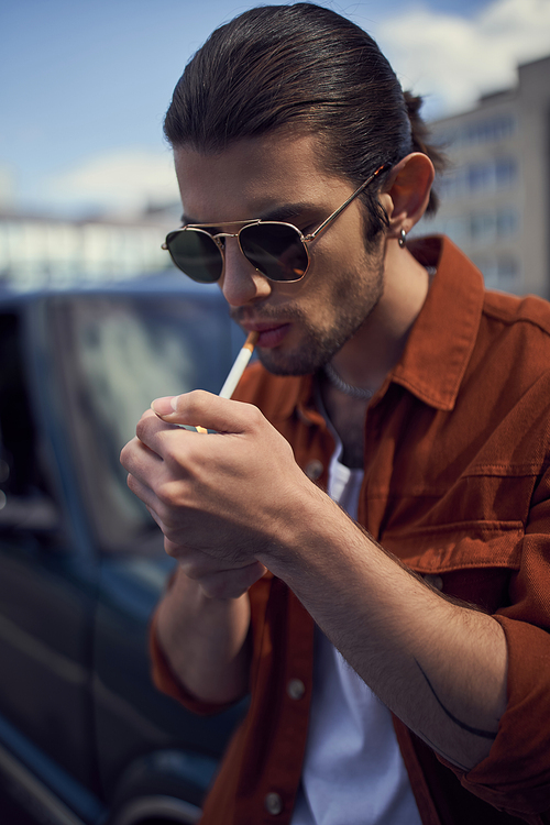 portrait of young stylish man with sunglasses lighting up his cigarette, vertical, style concept