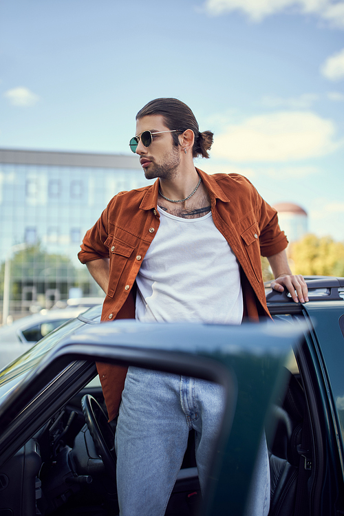 young charming male model posing in vibrant attire next to his car with opened door, style concept