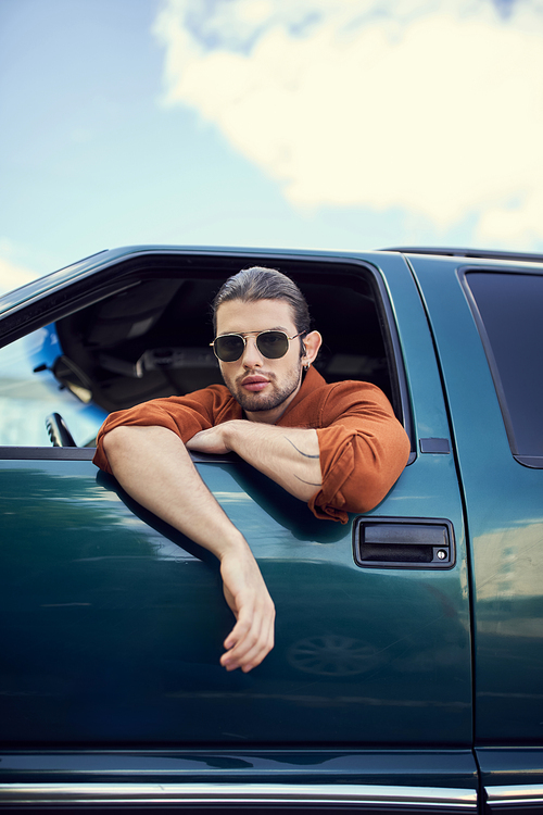 charming young man in brown shirt with sunglasses looking through car window, style and fashion