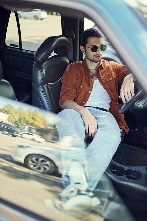 young stylish male model in brown shirt chilling behind driving steering wheel, fashion concept