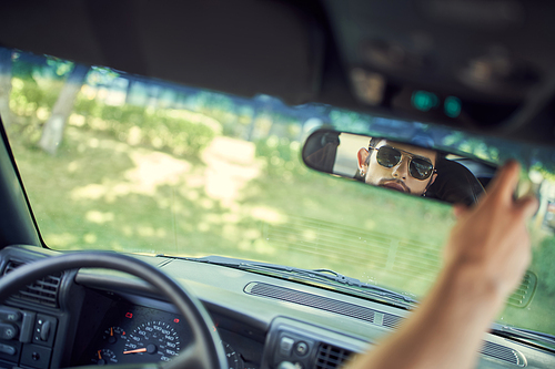 appealing man with stylish sunglasses looking at his rearview mirror, fashion and style