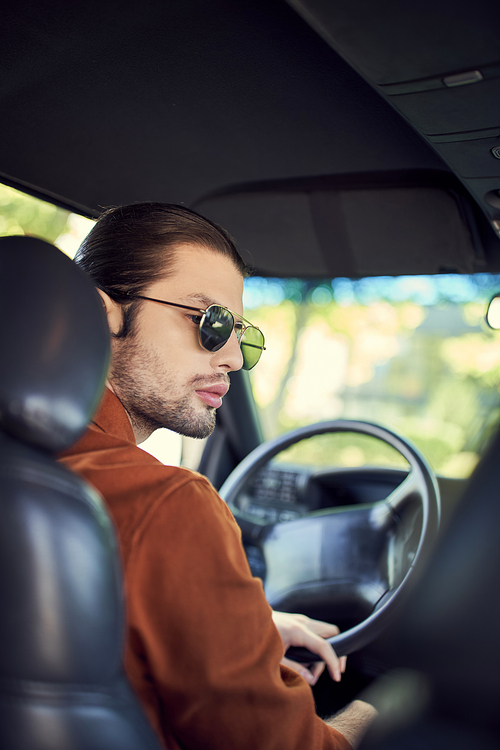 vertical shot of good looking sexy man in brown shirt with sunglasses and earring at steering wheel