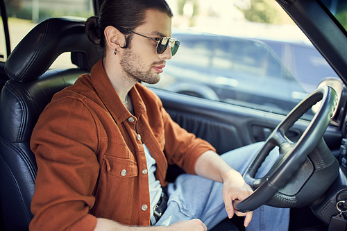 appealing young man in stylish vibrant outfit posing in profile in car while at steering wheel