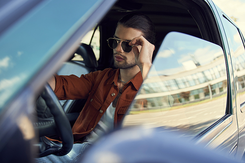 tempting young male model with elegant accessories and ponytail behind steering wheel, fashion