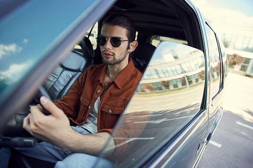 handsome young male model in stylish brown shirt with sunglasses at steering wheel, sexy driver