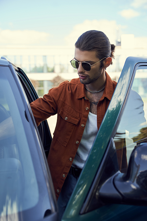 vertical shot of young attractive man in stylish outfit with sunglasses getting into car, fashion