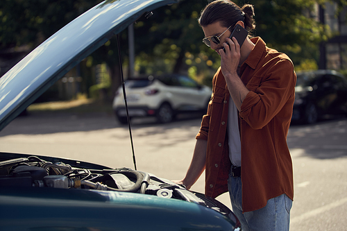 good looking sexy man in brown shirt talking to his insurer and looking at his car engine