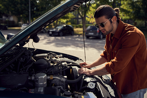 attractive stylish male model in trendy urban attire with accessories checking on his car engine