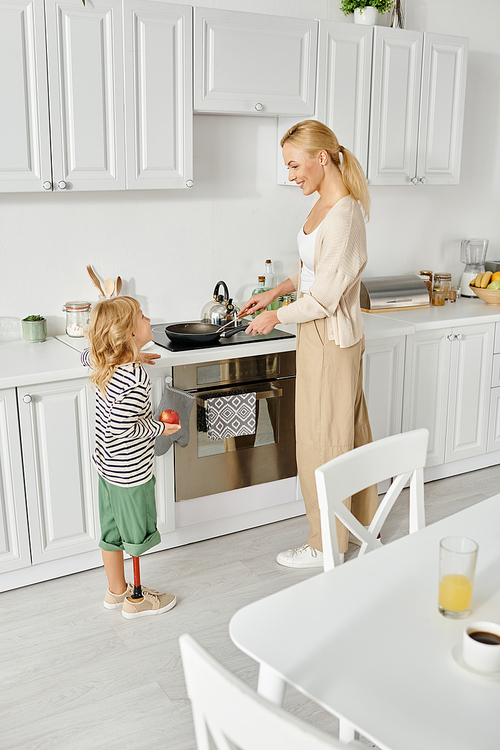 cute girl with prosthetic leg holding plate and helping happy mother washing dishes in kitchen