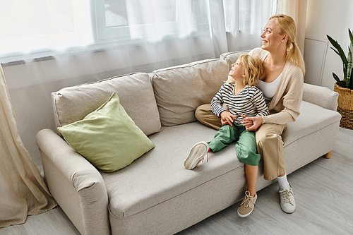 happy mother hugging daughter with prosthetic leg and sitting together on sofa in living room