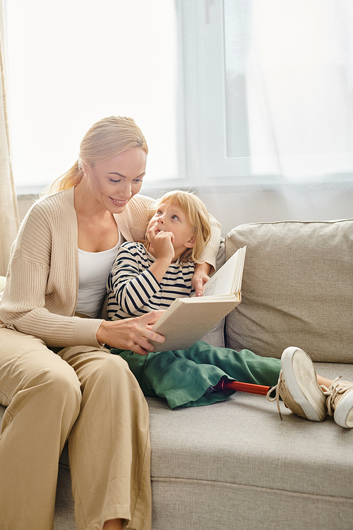 happy mother reading book to her blonde child with prosthetic leg, sitting together in living room