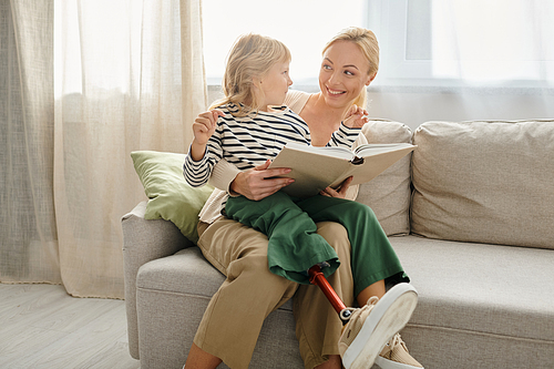 happy child with prosthetic leg sitting on laps of blonde mother and reading book in living room