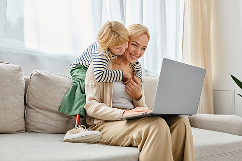 happy kid with prosthetic leg hugging blonde mother working on laptop in modern living room