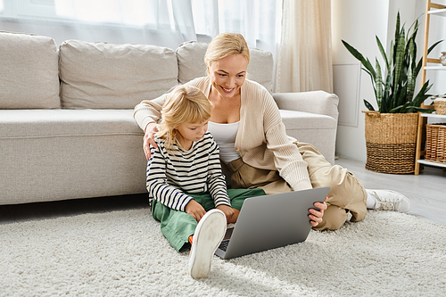 happy child with prosthetic leg using laptop and sitting on carpet with mother in living room