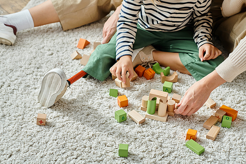 cropped shot, girl with prosthetic leg sitting on carpet and playing with wooden blocks near mother