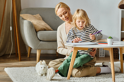 blonde girl with prosthetic leg drawing on paper with colorful pencils near supportive mother