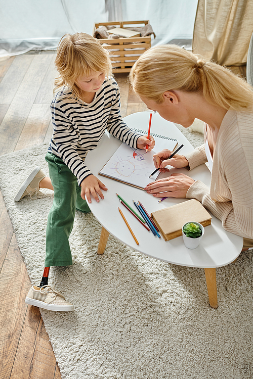 mother and child with prosthetic leg drawing together on paper with colorful pencils, quality time