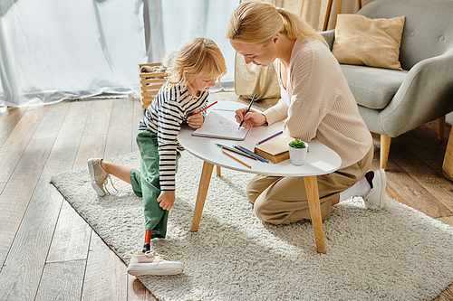 mother and daughter with prosthetic leg drawing on paper with colorful pencils, quality time