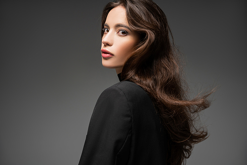 Trendy asian model with makeup and hairstyle posing in black jacket isolated on grey