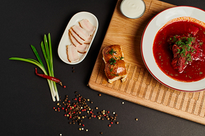 fresh Ukrainian beetroot soup near garlic buns, pork lard and green onions on cutting board on black