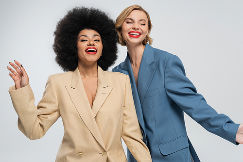 joyful and fashionable multiracial women posing in colorful suits on grey backdrop, diverse beauty