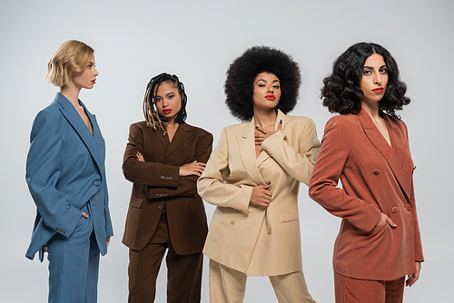 glamorous multiracial female models in stylish colorful suits on grey, diversity and fashion