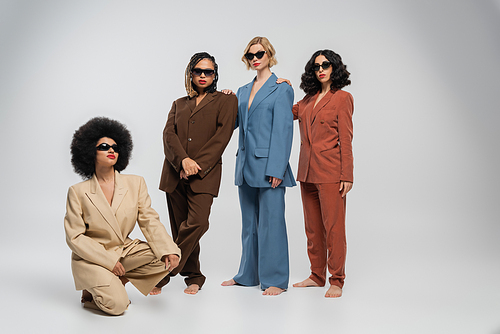 african american woman sitting on haunches near multiracial girlfriends in sunglasses and suits