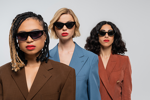 group portrait of trendy multiracial girlfriends in dark sunglasses and colorful suits on grey