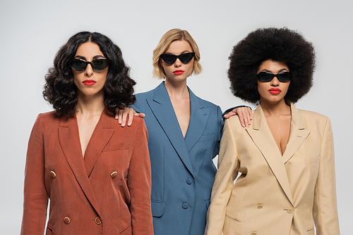 diversity and style, multicultural women in trendy colorful suits and dark sunglasses on grey