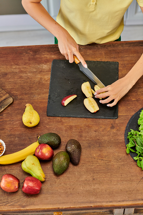 top view of cropped woman cutting apple near fresh fruits on wooden table, healthy plant-based diet