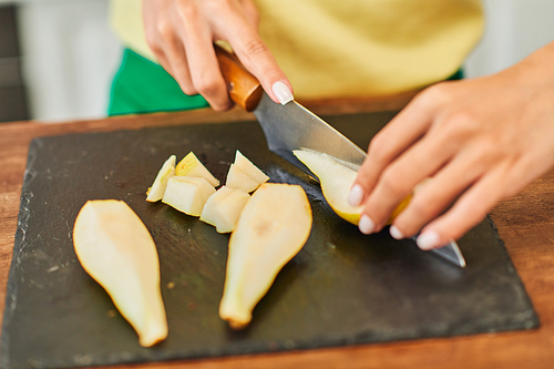 cropped view of woman cutting ripe fresh pear on chopping board, plant-based culinary concept