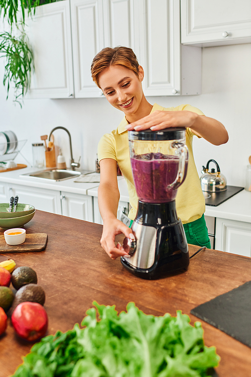 delighted vegetarian woman grinding fresh fruits in electric blender, delicious smoothie recipe