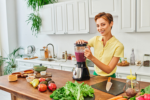 vegetarian woman preparing smoothie in electric blender near fresh fruits and vegetables in kitchen