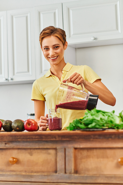 vegetarian culinary delight, happy young woman pouring fresh smoothie from blender into mason jar