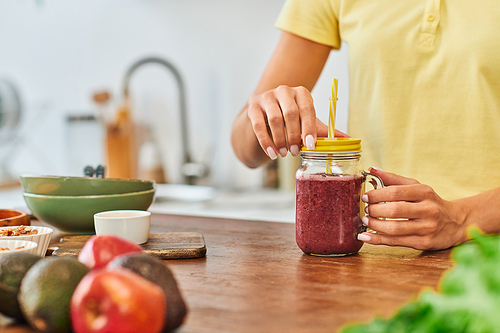 cropped view of woman near mason jar with delicious plant-based smoothie near blurred fresh fruits