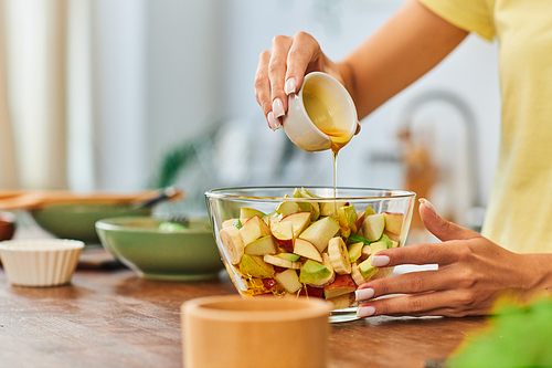 partial view of woman pouring honey on wholesome fruit salad in glass bowl, plant-focused diet