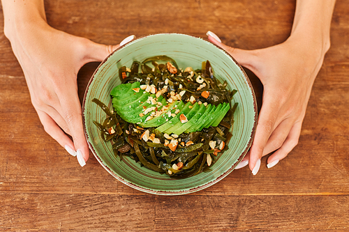 top view of female hands near salad with seaweed and sliced avocado with walnuts, vegetarian recipe