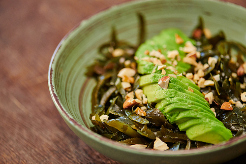 close up view of vegetarian salad with seaweeds and sliced avocado with walnuts on wooden table