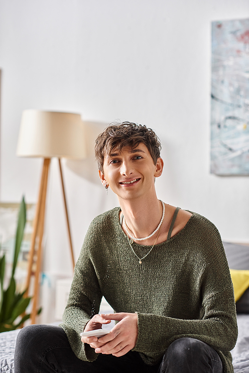 happy transgender person in casual attire looking at camera and sitting in modern apartment