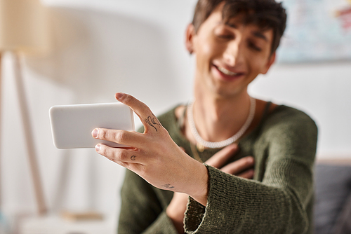 happy curly transgender influencer smiling using smartphone during online streaming, social media