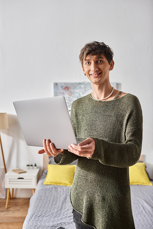 transgender blogger with curly hair using laptop while standing in modern apartment, influencer